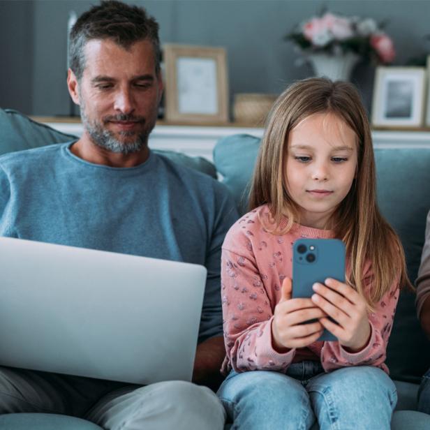 Eine Familie sitzt mit Notebook, iPhone und iPad auf der Couch.