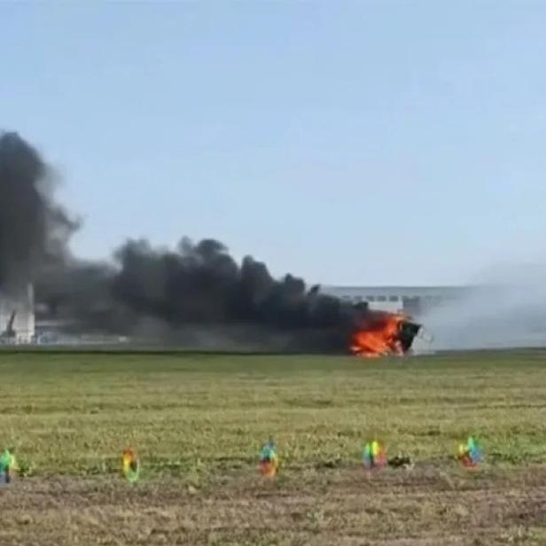 Ein brennendes Fahrzeug steht auf einer Wiese.