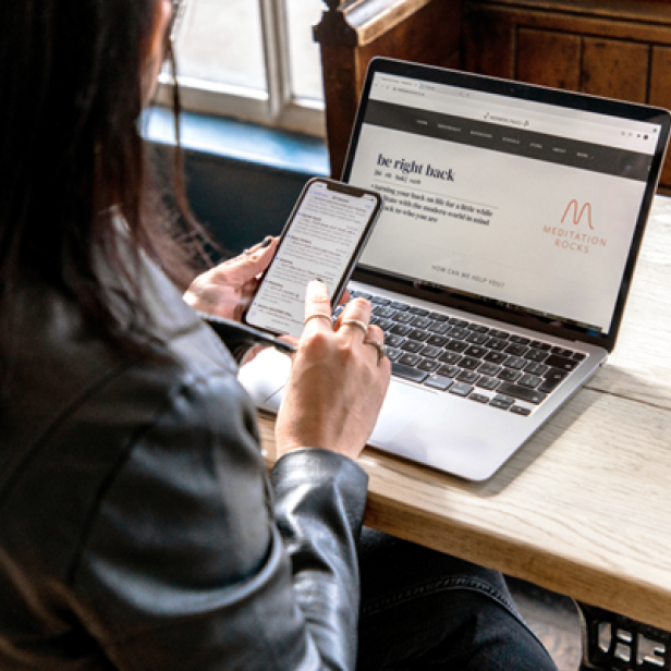 Eine Frau sitzt an einem Laptop und ist an ihrem Handy.