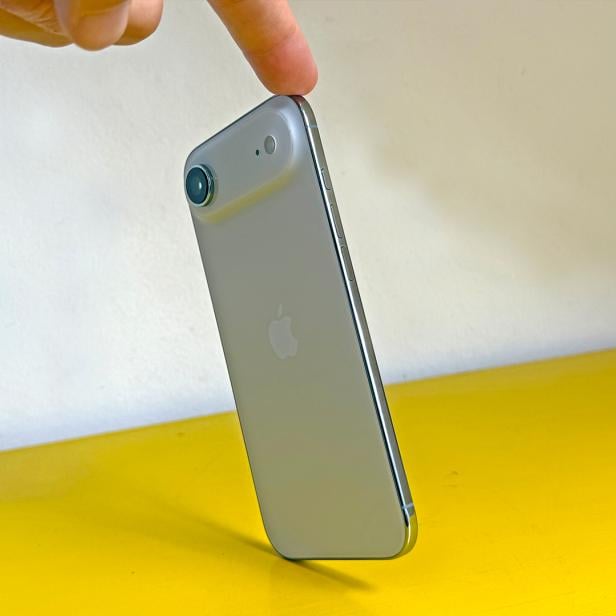 Ein Finger berührt ein silbernes iPhone auf einem gelben Tisch.