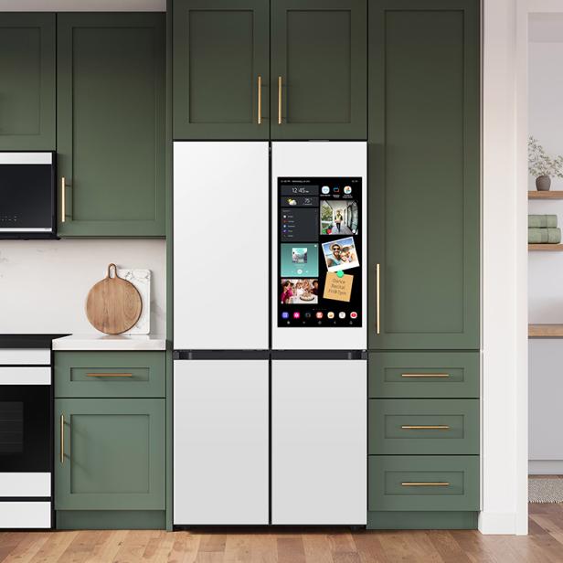 Moderne Küche mit grünen Schränken, weißen Arbeitsflächen, einem smarten Kühlschrank und Holzregalen mit Geschirr.