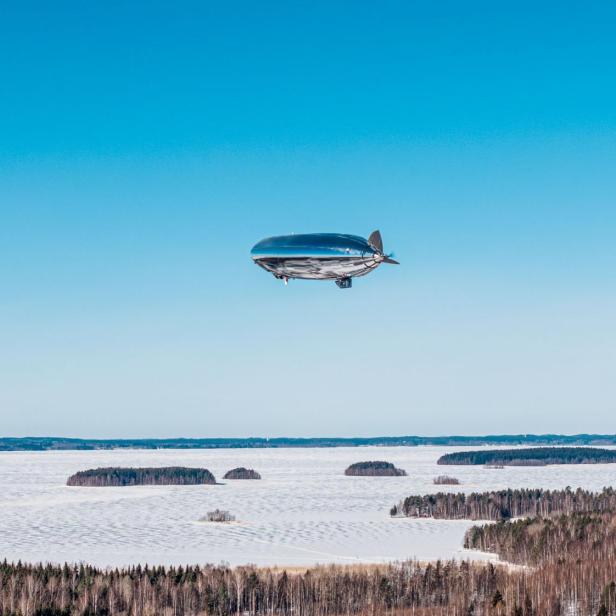 Ein silbernes Luftschiff fliegt über eine verschneite Wald- und Seenlandschaft.