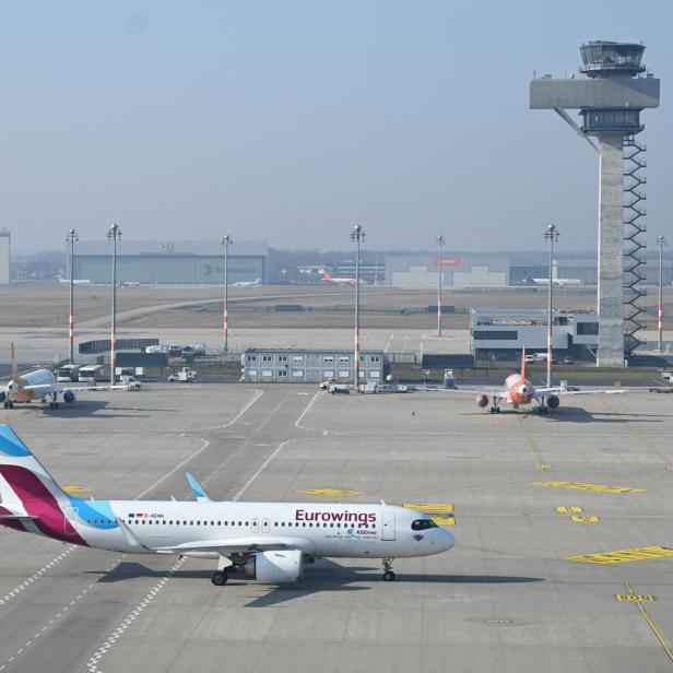 Ein Flugzeug von Eurowings rollt auf dem Vorfeld eines Flughafens, im Hintergrund steht ein hoher Kontrollturm.