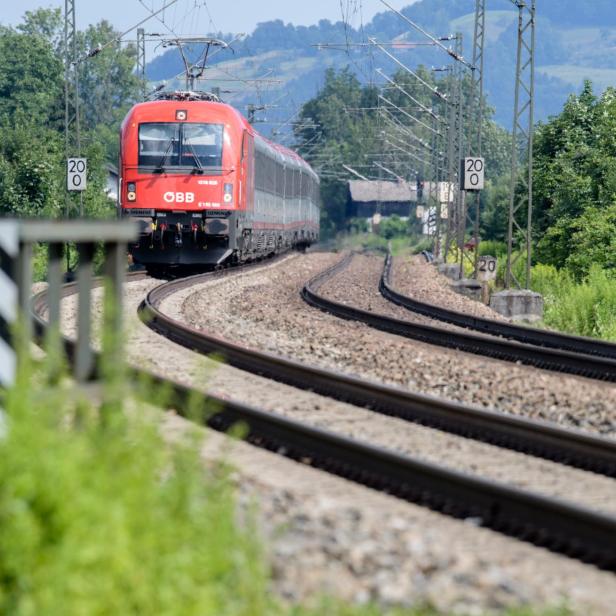 Ein roter Zug der ÖBB fährt auf einer kurvigen Bahnstrecke durch eine grüne, ländliche Landschaft.