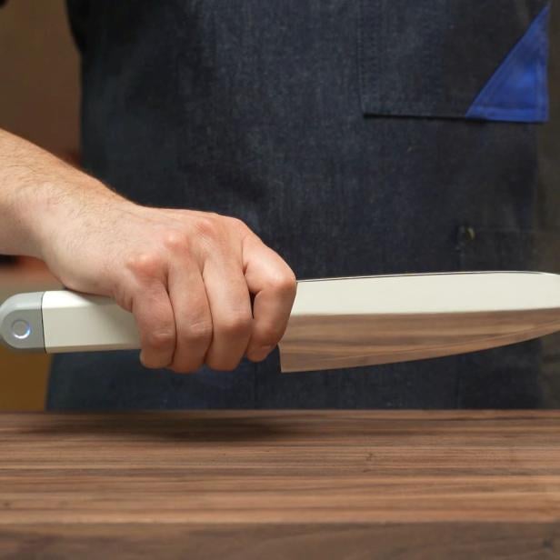 eine Hand hält das Messer über einer hölzernen Arbeitsplatte