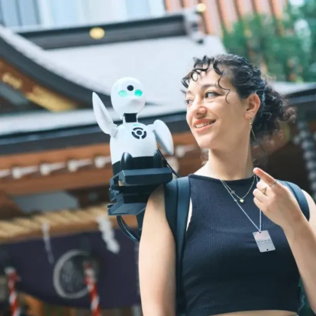 Eine Touristin mit dem Roboter OriHime auf der Schulter.