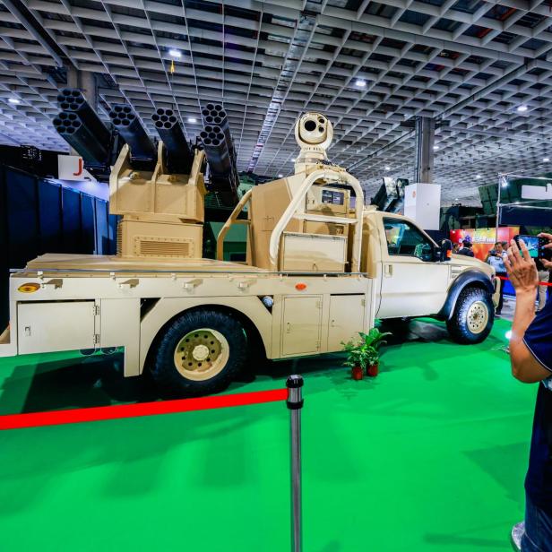 Ein Mann fotografiert ein militärisches Fahrzeug mit Raketenwerfern und Überwachungstechnik auf einer Messe.