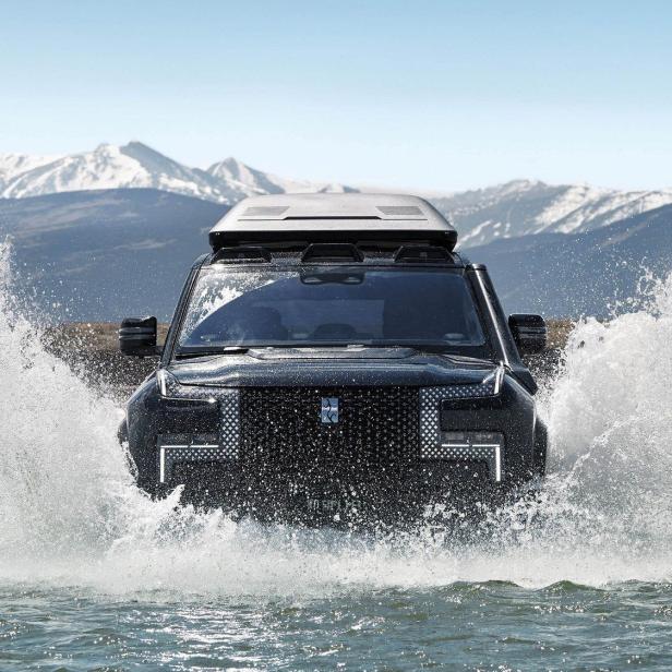 Ein schwarzer Geländewagen fährt durch ein Gewässer.