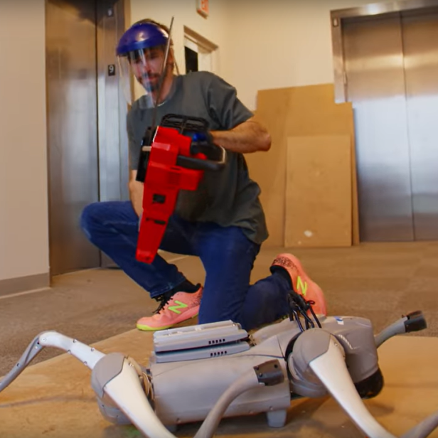 Ein Mann hält eine Kettensäge in der Hand bevor er die Beine eines Roboters absägt