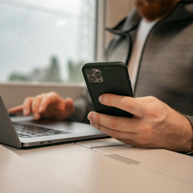 Person sitzt mit Laptop und Smartphone an einem Tisch