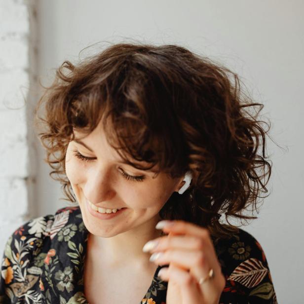 Eine junge Frau mit lockigen Haaren lächelt und trägt kabellose Ohrhörer.