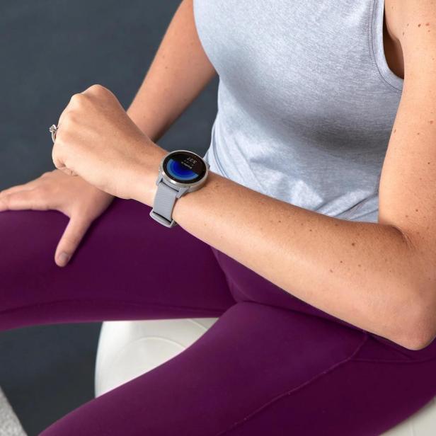 Frau in Sportkleidung sitzt und schaut auf eine graue Sportuhr von garmin