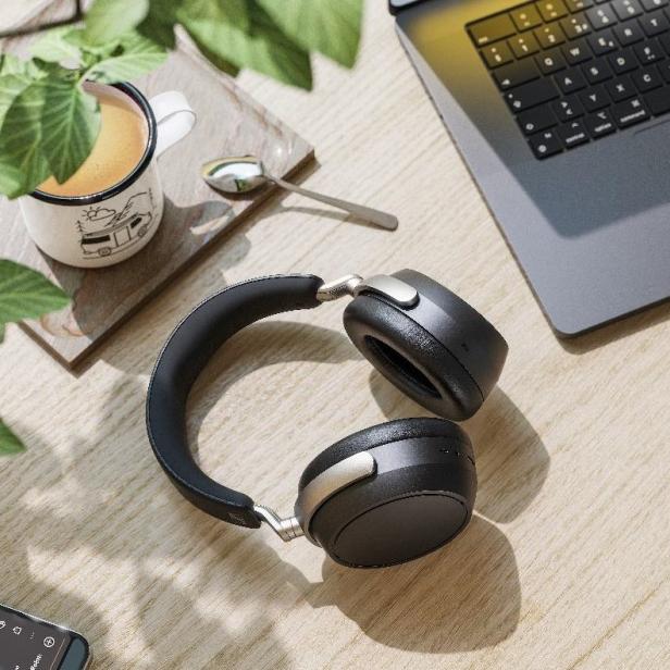 Der Sennheiser HDB 630 Kopfhörer liegt auf einem Schreibtisch neben einem Laptop, einer Tasse Kaffee und einem Smartphone mit geöffneter Musik-App.