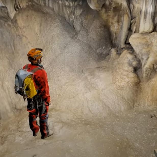 Screenshot des 3D-Modell-Videos einer Höhle, darauf eine Person in rot-oranger Höhlenausrüstung