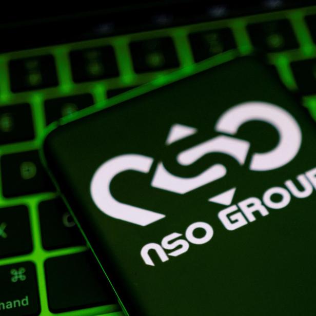 NSO Group Logo auf einem Smartphone, dass vor grün beleuchteter Computertastatur liegt
