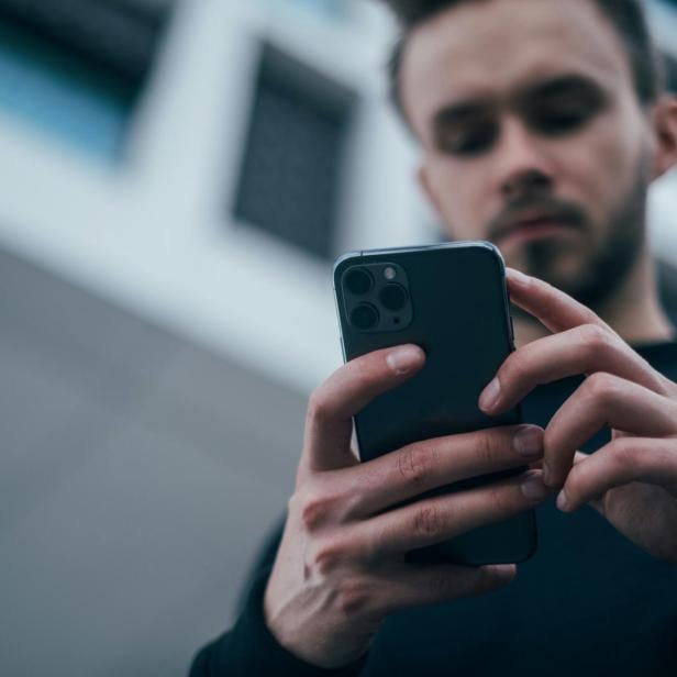 Ein junger Mann nutzt ein Smartphone, während OpenAI neue ChatGPT-Funktionen für erwachsene Nutzer ankündigt.