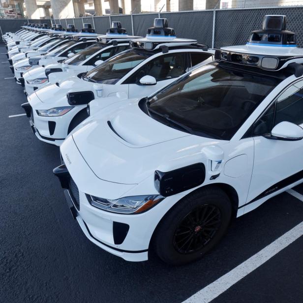 Eine Reihe weißer Waymo-Fahrzeuge mit Sensoren auf dem Dach stehen geparkt.