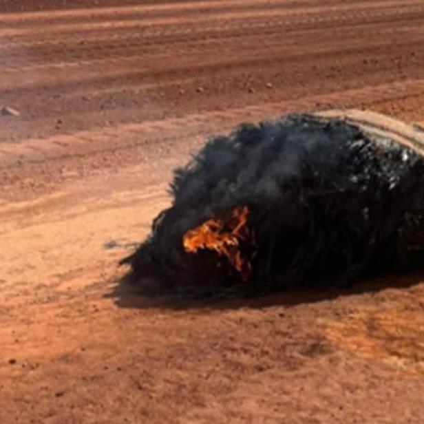Ein brennendes, verkohltes Objekt liegt auf sandigem Wüstenboden und wird als mutmaßlicher Weltraumschrott identifiziert.