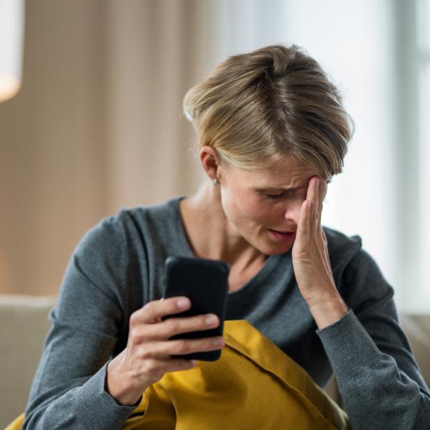 Eine verzweifelte Frau sitzt auf der Couch vor ihrem Smartphone