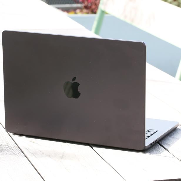 MacBook Pro 14 Zoll in dunkler Farbe auf einem Holztisch im Freien.