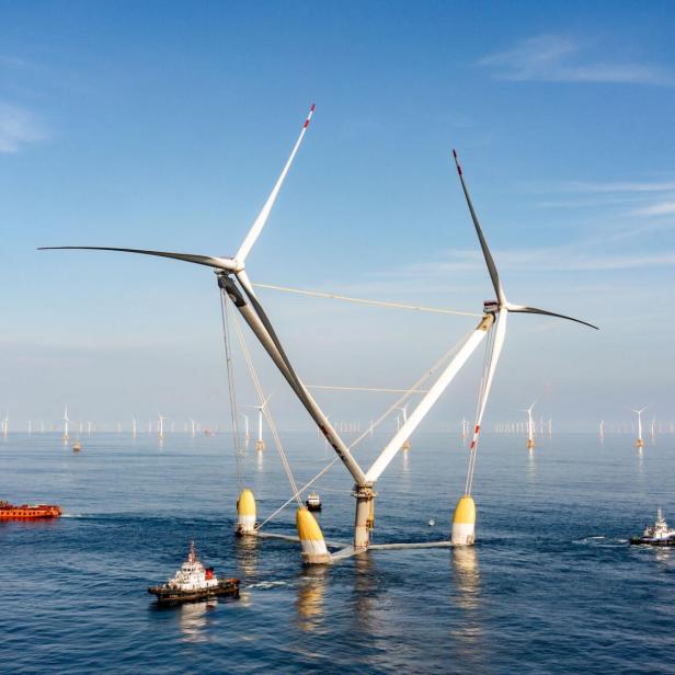 Die schwimmende Offshore-Windkraftanlage OceanX von Mingyang mit zwei V-förmig angeordneten Rotoren wird von mehreren Schiffen auf dem Meer begleitet.