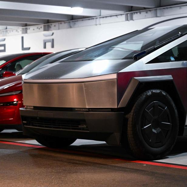 Ein Tesla Cybertruck steht neben einem roten Tesla in einer Garage unter dem Tesla-Schriftzug.