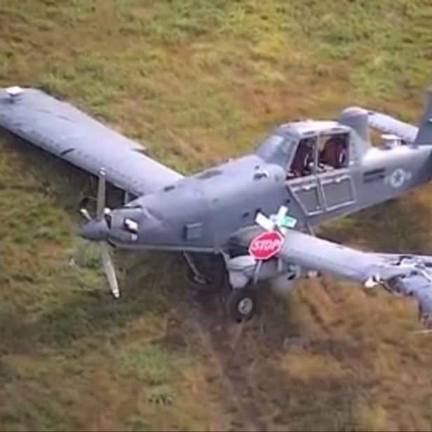 Beschädigtes Militärflugzeug mit abgebrochener Tragfläche und Stoppschild auf Wiese.
