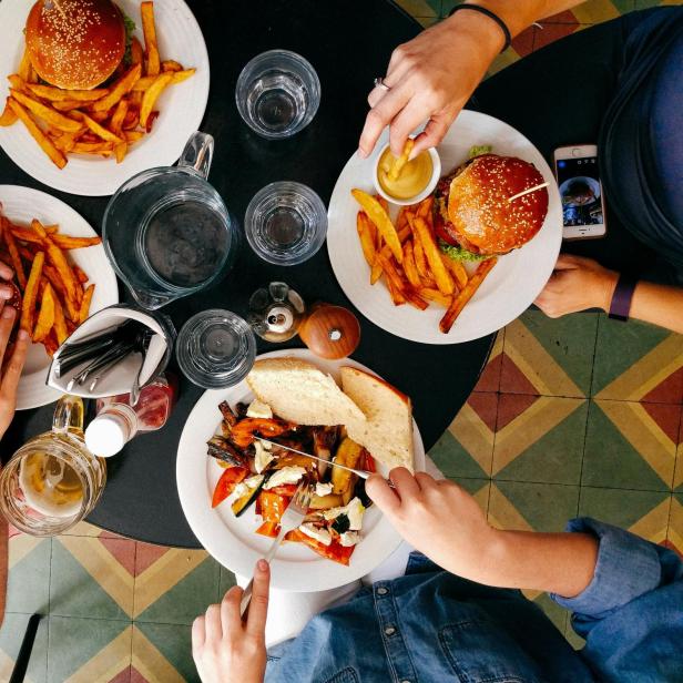 Menschen sitzen an einem Tisch und haben Burger und Salat vor sich 