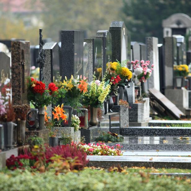 Reihe von Grabsteinen mit vielen bunten Blumensträußen und Pflanzen auf den Gräbern.