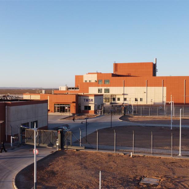 Das TMSR-Gebäude mit Zaun steht in einer weiten, offenen Landschaft unter blauem Himmel.