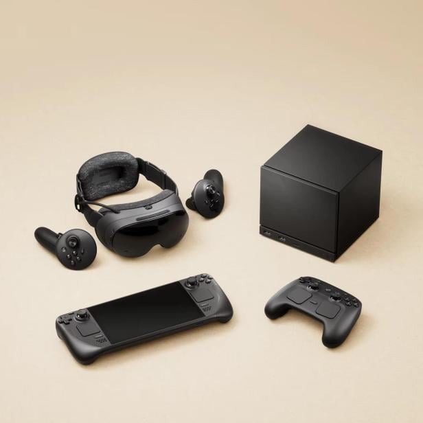 Auf beigem Grund liegen eine VR-Brille, zwei Controller, ein Steam Deck und eine schwarze Box.