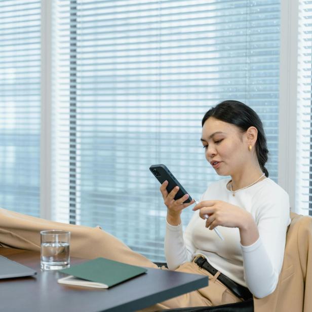 Eine Frau, die ihre Füße auf dem Schreibtisch liegen hat, hält ein Smartphone in der Hand 