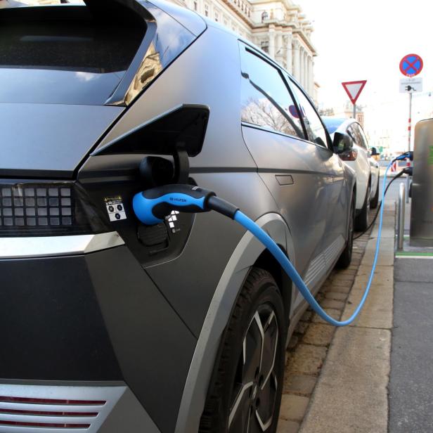 Ein Elektroauto wird an einer öffentlichen Ladestation mit einem blauen Kabel aufgeladen.