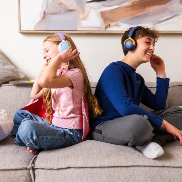 Zwei Kinder sitzen lachend auf einem Sofa und tragen die myFirst CareBuds Max Kopfhörer in verschiedenen Farben.