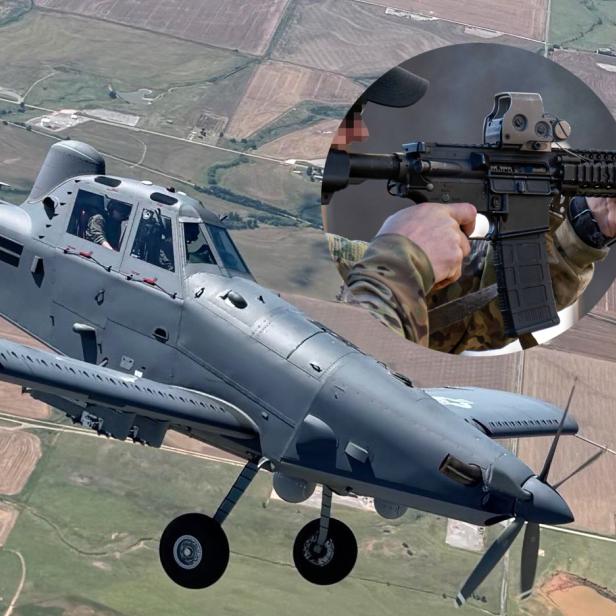 Ein graues Militärflugzeug der US-Luftwaffe fliegt über Felder, im Kreis ist ein Soldat mit einem Sturmgewehr zu sehen.