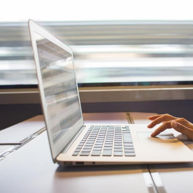 Eine Person arbeitet an einem Laptop auf einem Tisch in einem fahrenden Zug.