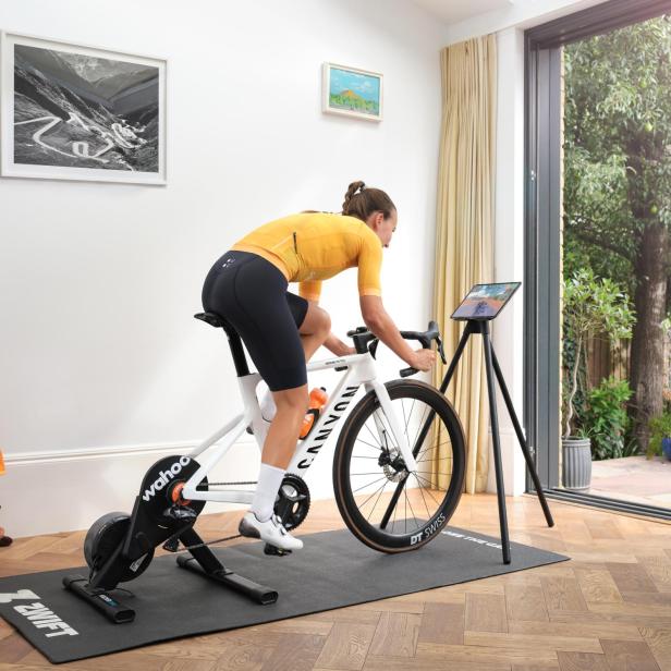 Eine Frau trainiert auf einem Canyon-Rennrad mit Wahoo-Smarttrainer und nutzt die Zwift-App auf einem Tablet im Wohnzimmer.