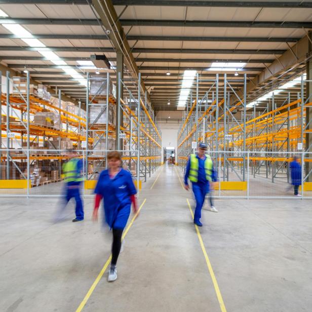 Personen gehen vor Lagerregalen 