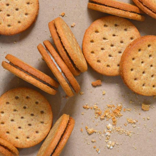 Mehrere Doppelkekse und Keksbrösel auf braunem Untergrund.