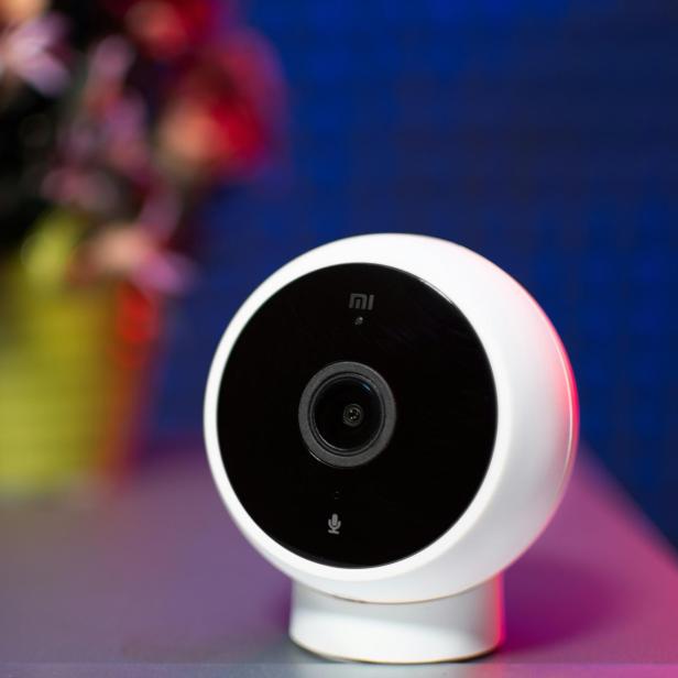 Weiße Überwachungskamera auf Tisch, im Hintergrund ein unscharfer Blumenstrauß.