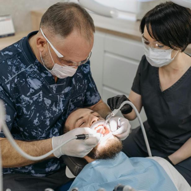 Zahnarzt behandelt einen Patienten, während eine Assistentin daneben sitzt und hilft.