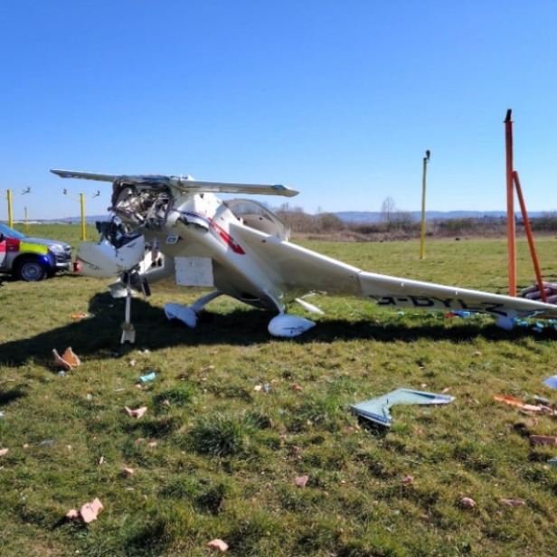 Ein beschädigtes Kleinflugzeug liegt auf einer Wiese neben Trümmern und einem Einsatzfahrzeug.