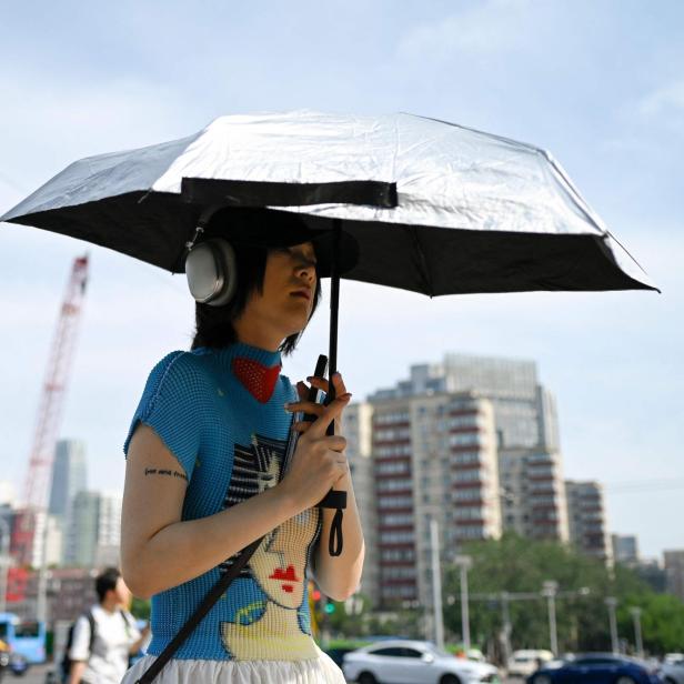 Eine Person mit Kopfhörern hält einen silbernen Regenschirm in einer städtischen Umgebung.