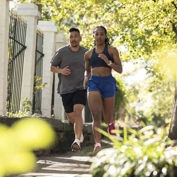 Zwei Personen joggen auf einem sonnigen Weg mit Bäumen.