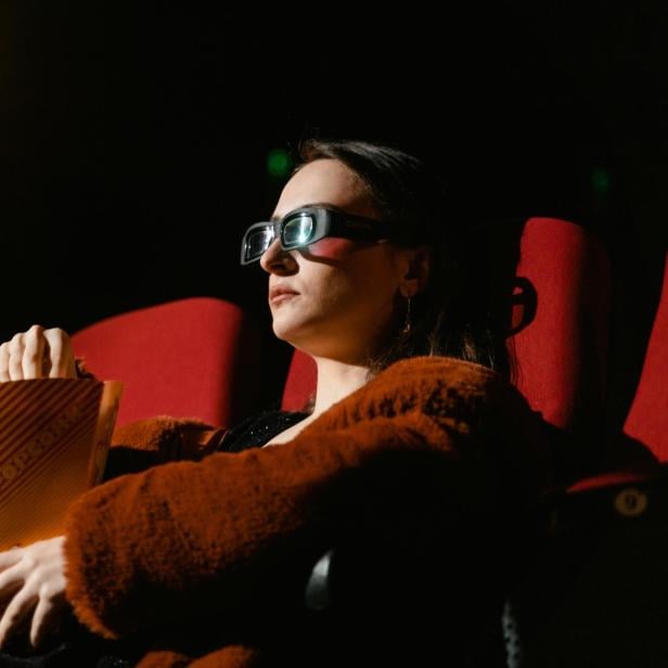 Frau mit 3D-Brille sitzt im Kinosessel und hält eine Popcorntüte.