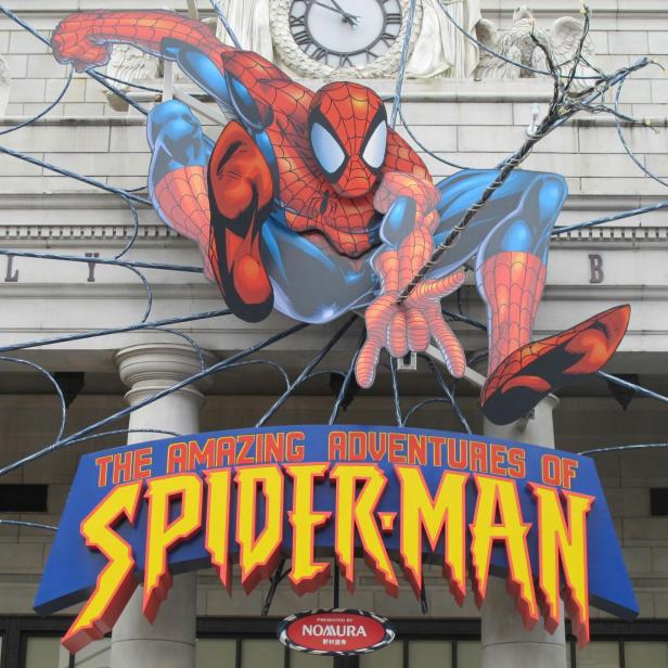 Eine große Spider-Man-Figur mit Spinnennetz und dem Schriftzug „The Amazing Adventures of Spider-Man“ vor einem Gebäude mit Uhr.