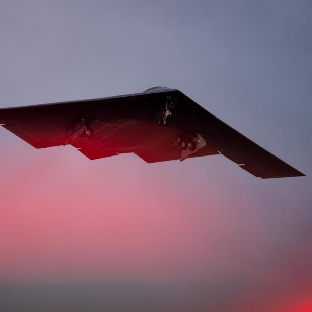 B-2 Stealth-Bomber im Flug bei Sonnenuntergang mit ausgefahrenem Fahrwerk.