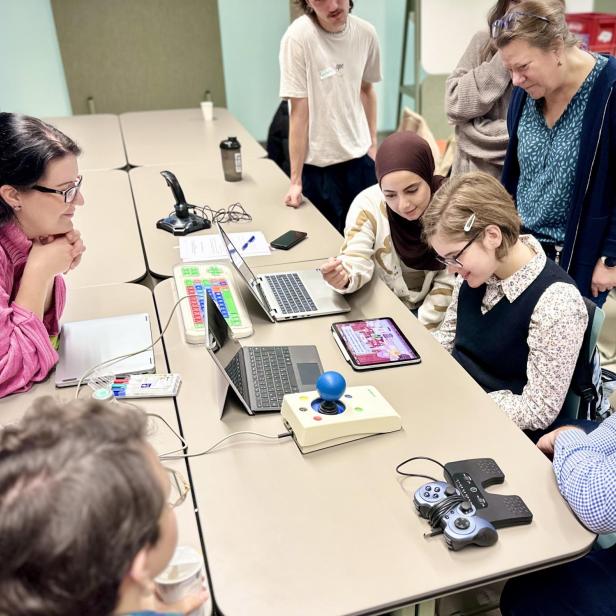 Mehrere Personen testen gemeinsam an einem Tisch technische Hilfsmittel und Tablets.