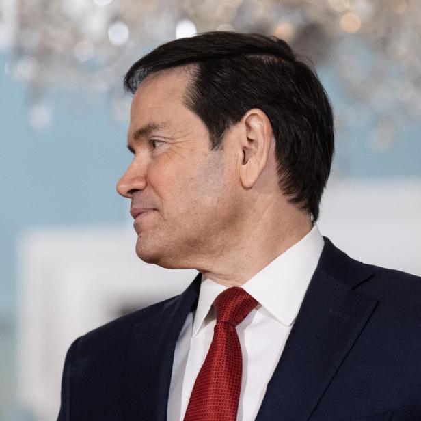 US Secretary of State Rubio  im dunklen Anzug und roter Krawatte blickt zur Seite.