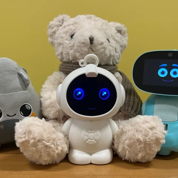 Vier verschiedene KI-Spielzeuge, darunter Plüschtiere und Roboter, auf einem Holztisch.